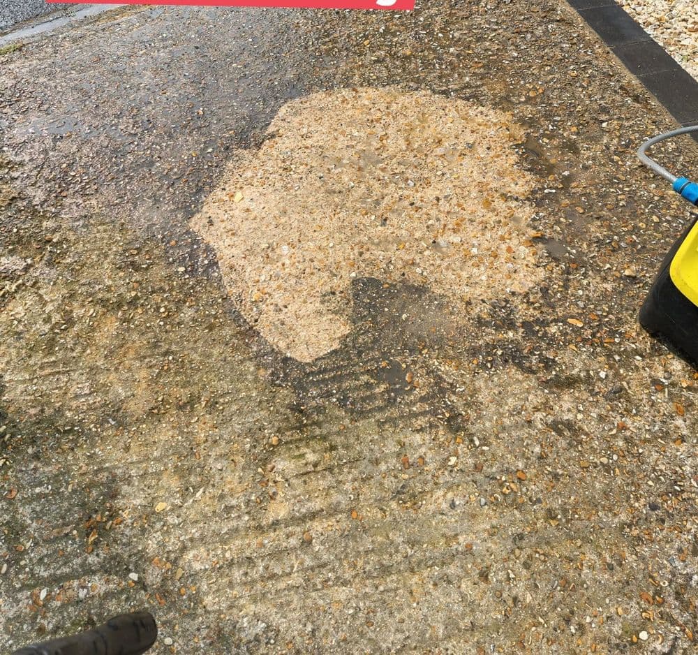A pressure-washer test patch on a grimy driveway, showing clean stone against the dirt around it
